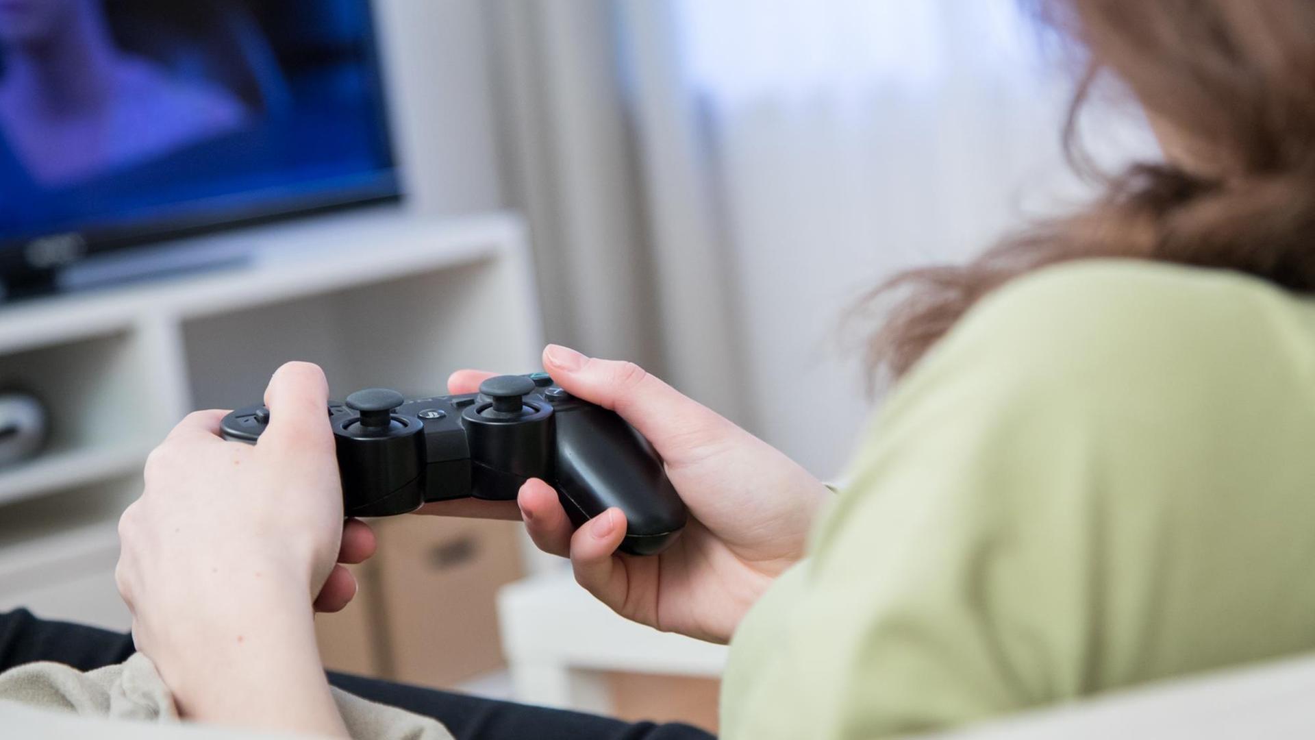 Eine junge Frau sitzt in einer Wohnung und spielt Videospiele eber das Fernsehgeraet. (Symbolbild)