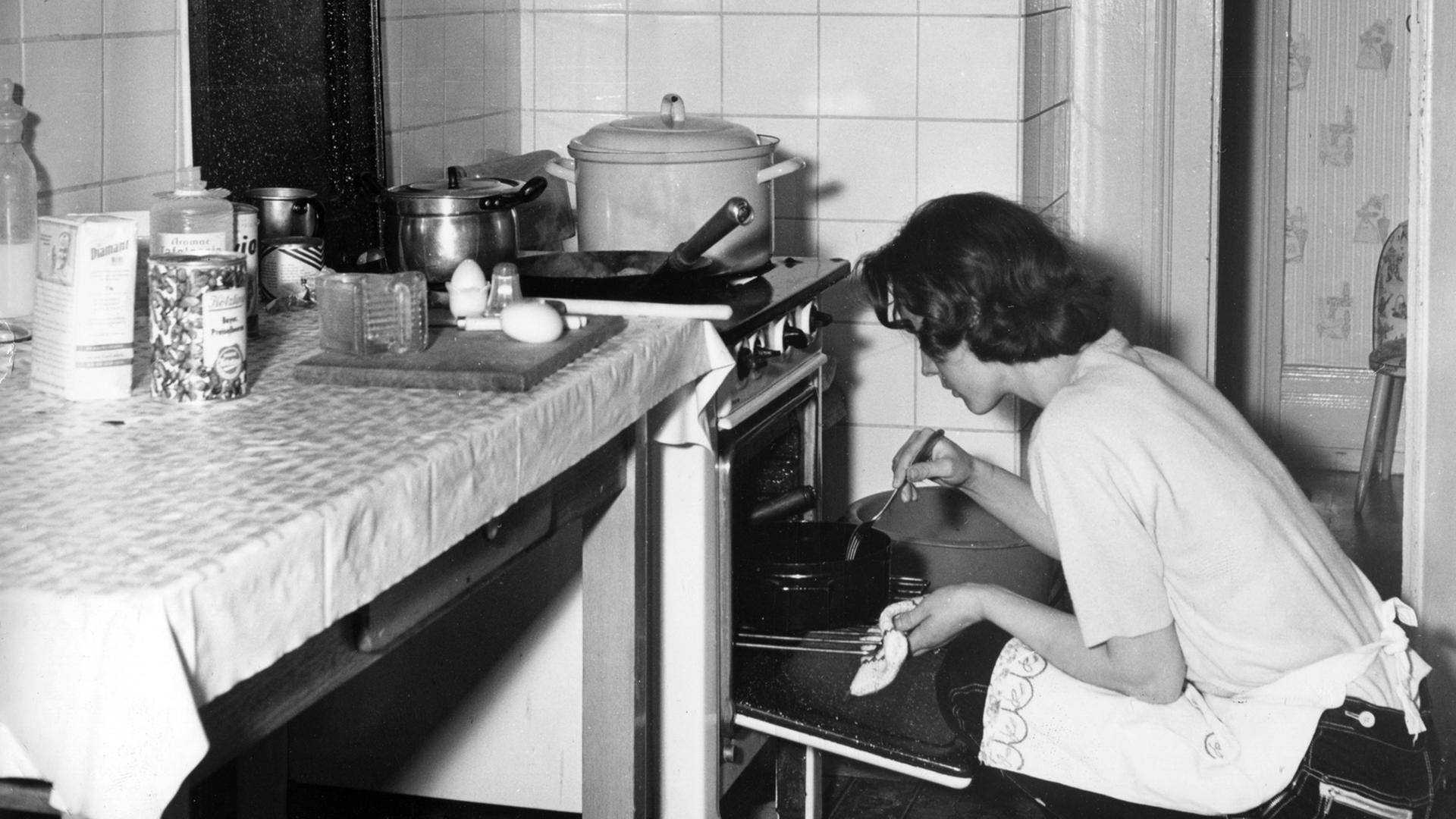 Undatierte Aufnahme aus den 1950er oder 1960er Jahren: Eine junge Hausfrau kniet vor einem Ofen und kontrolliert einen Braten. Undatierte Aufnahme aus den 1950er oder 1960er Jahren: Eine junge Hausfrau kniet vor einem Ofen und kontrolliert einen Braten.