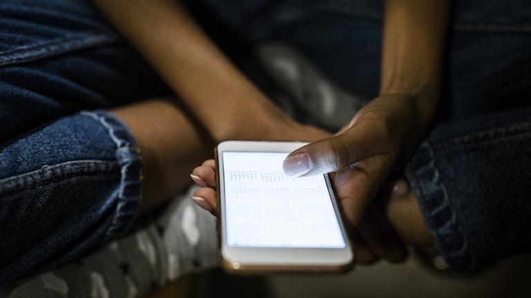 Bezahlen mit dem Handy ist durch M-Pesa in vielen afrikanischen Ländern zum Standard geworden. Eine junge Frau wischt mit dem Finger über das helle Handy-Display.