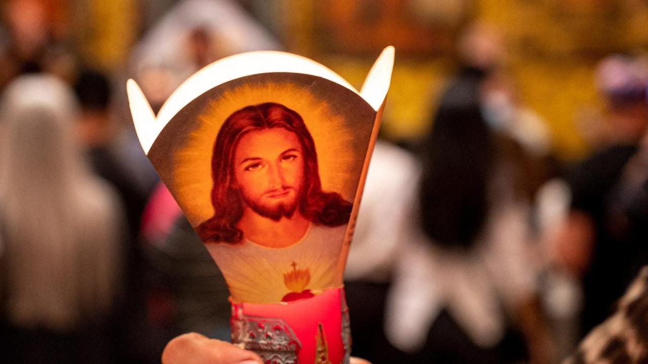 In einer Kirche hält eine Gläubige eine Kerze, die mit dem Bild von Jesus verziert ist.