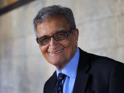 Amartya Sen steht vor einer Mauer und schaut freundlich in die Kamera.
