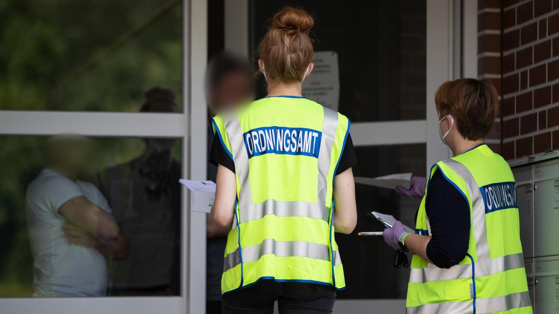 19.06.2020, Nordrhein-Westfalen, Rheda-Wiedenbrück: Mitarbeiter des Ordnungsamtes sprechen mit ausländischen Bewohnern einer Unterkunft, die im fleischproduzierenden Gewerbe arbeiten. Beim Schlachtereibetrieb Tönnies in Rheda-Wiedenbrück sind seit Anfang der Woche mehrere hundert Mitarbeiter positiv auf das Coronavirus getestet worden. Foto: Friso Gentsch/dpa | Verwendung weltweit 19.06.2020, Nordrhein-Westfalen, Rheda-Wiedenbrück: Mitarbeiter des Ordnungsamtes sprechen mit ausländischen Bewohnern einer Unterkunft, die im fleischproduzierenden Gewerbe arbeiten. Beim Schlachtereibetrieb Tönnies in Rheda-Wiedenbrück sind seit Anfang der Woche mehrere hundert Mitarbeiter positiv auf das Coronavirus getestet worden. Foto: Friso Gentsch/dpa | Verwendung weltweit