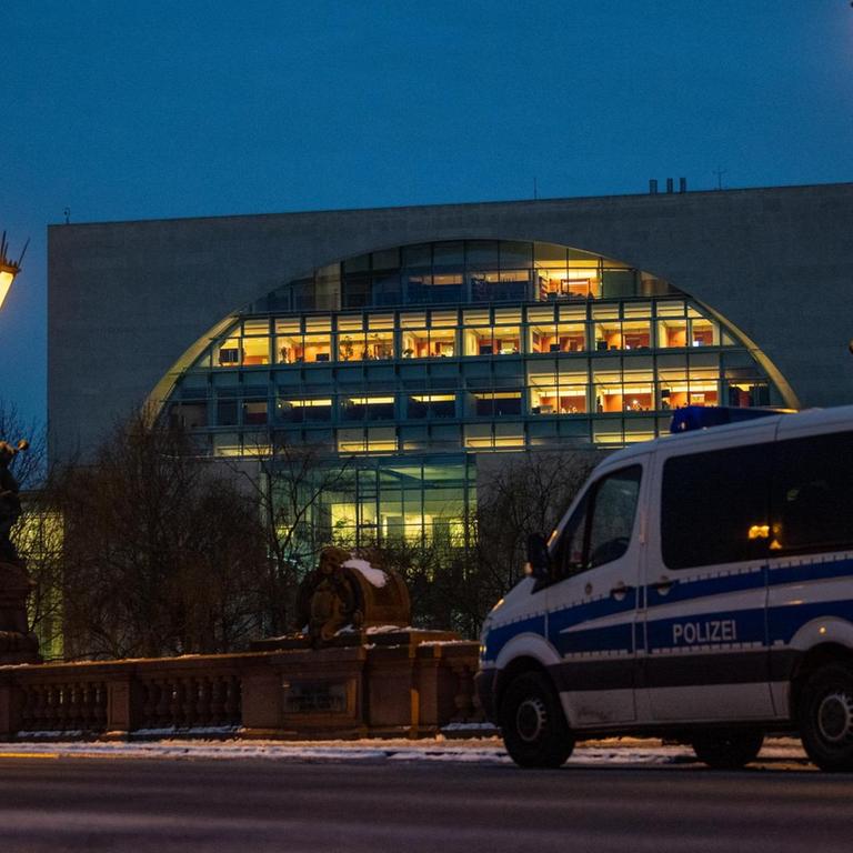 Ein Polizeifahrzeug steht vor dem beleuchteten Bundeskanzleramt
