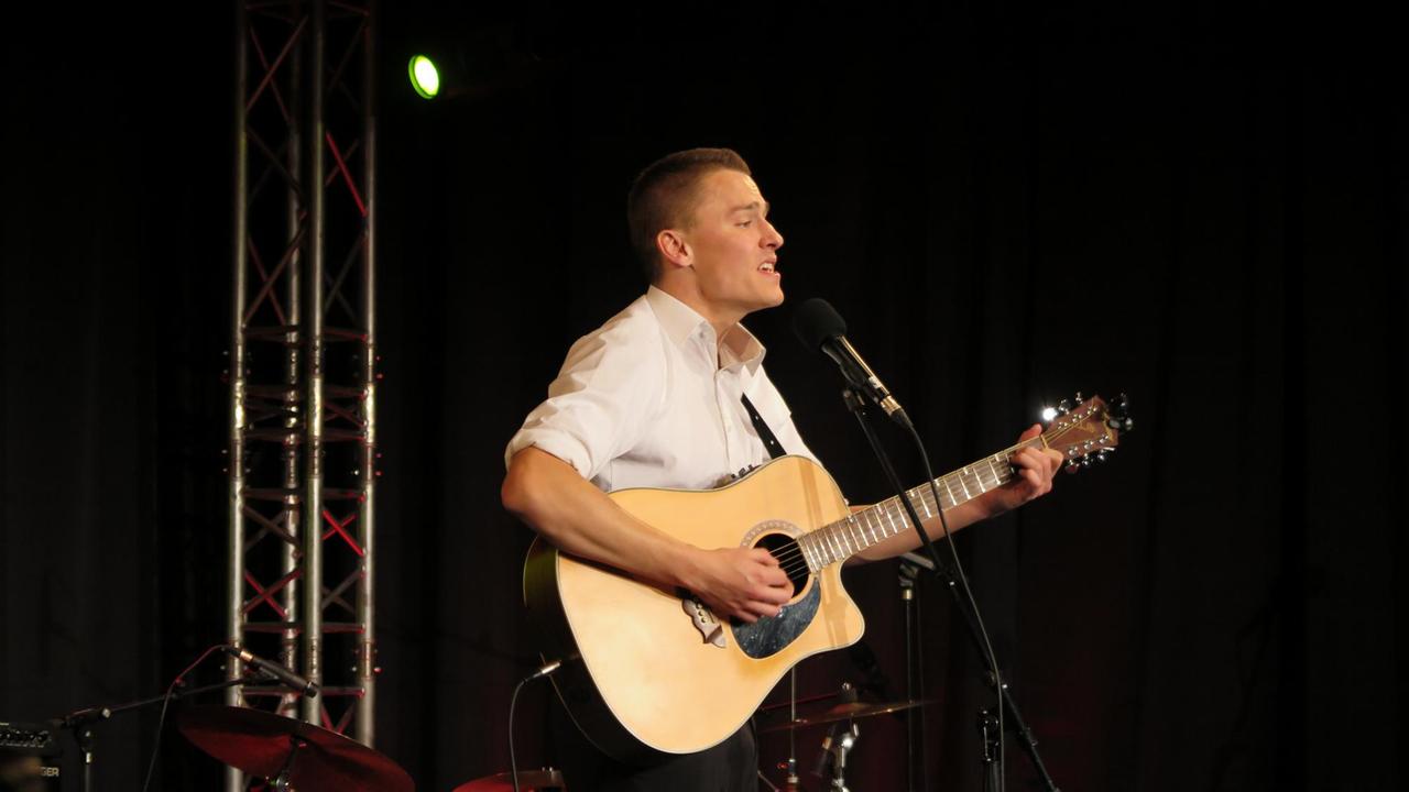 Alex Döring singt zur Gitarre vor dunklem Bühnenhintergrund Alex Döring singt zur Gitarre vor dunklem Bühnenhintergrund