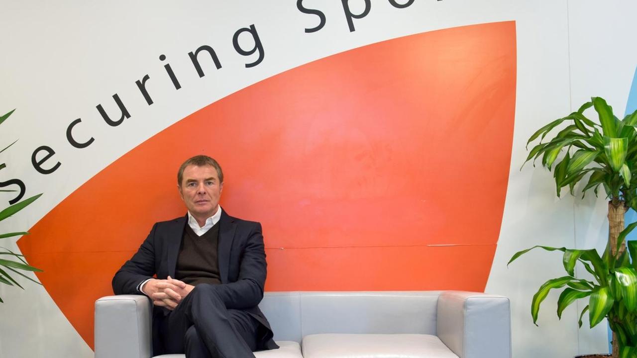 Spahn sitzt auf einer Bank zwischen zwei Grünpflanzen. Auf der Wand hinter ihm steht "Securing Sport".