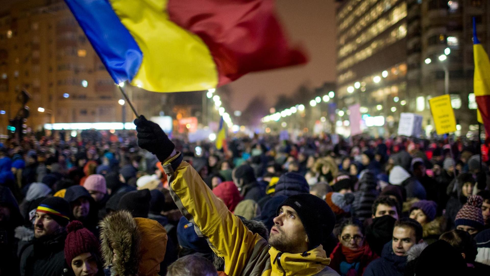 In einer großen Menschenmenge schwenkt ein Demonstrant die rumänische Flagge. In einer großen Menschenmenge schwenkt ein Demonstrant die rumänische Flagge.