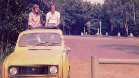 Günther Wessel mit seinem Renault 1977. Ein Pärchen schaut aus dem Dachfenster eines gelben Renaults.
