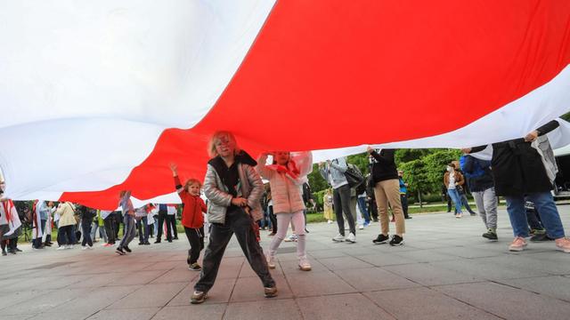 Demonstranten halten eine grosse traditionelle rotweisse belarussische Flagge in Vilnius, Kinder laufen darunter. Weiß-Rot-Weiß sind die Farben der Opposition. Sie fordern Freiheit für den Journalisten Roman Protasevich. 23. Mai 2021.