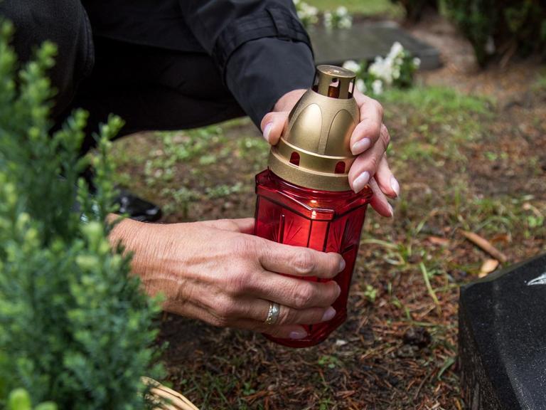 Eine Frau zündet in Hamburg auf einem Friedhof eine Kerze an.