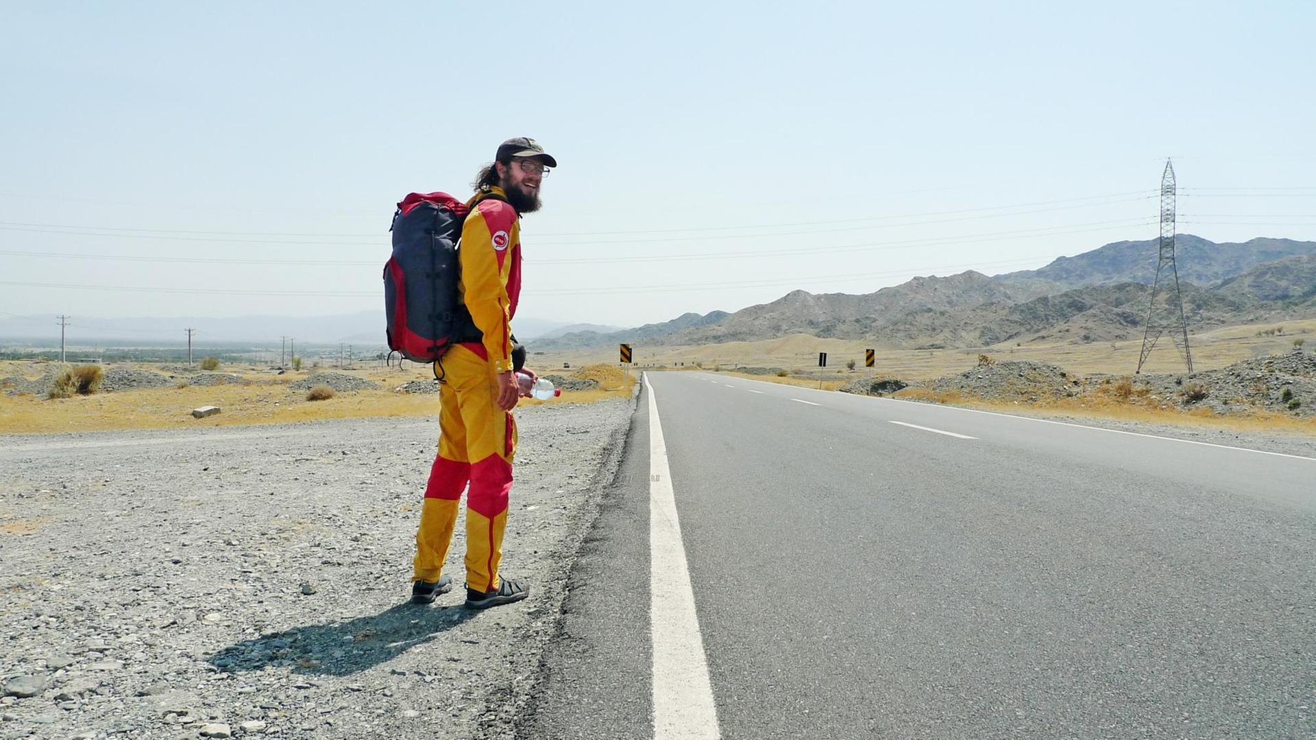 Der Protagonist Stefan läuft, in einem gelb-roten Overall, allein an einer Straße entlang.