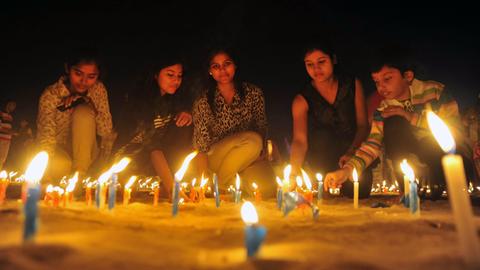 Feierlichkeiten zum indischen Diwali Festival: junge Menschen zünden auf dem Boden stehende Kerzen an