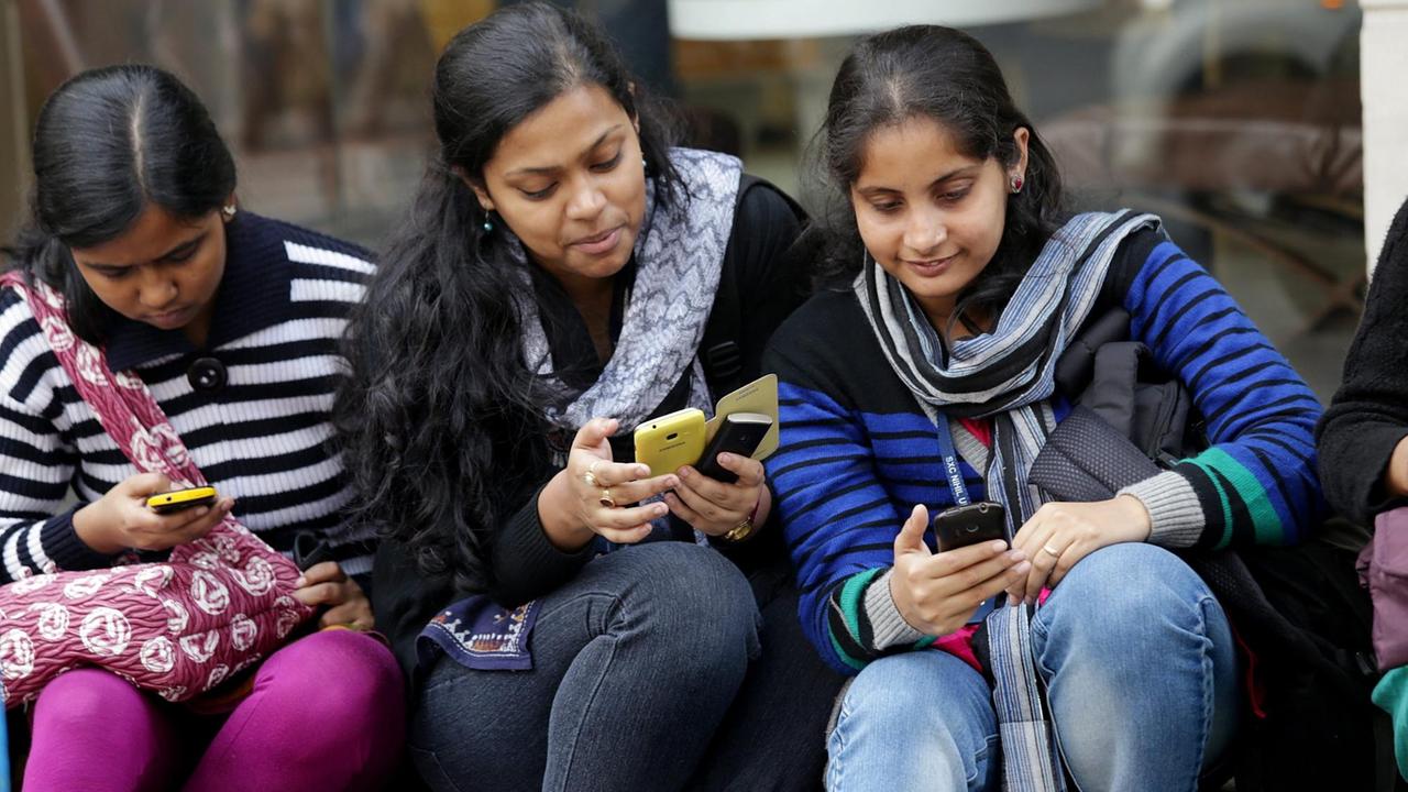 Derei junge Inderinnen in Kalkutta schauen auf ihre Smartphones. Derei junge Inderinnen in Kalkutta schauen auf ihre Smartphones.