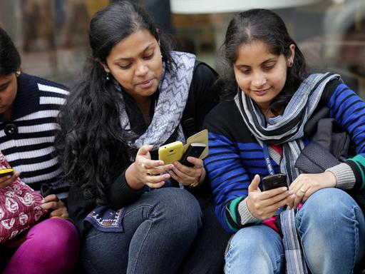 Derei junge Inderinnen in Kalkutta schauen auf ihre Smartphones