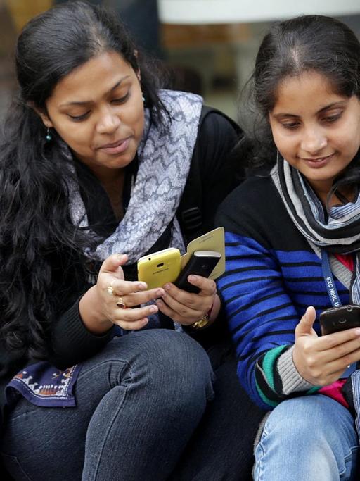 Derei junge Inderinnen in Kalkutta schauen auf ihre Smartphones