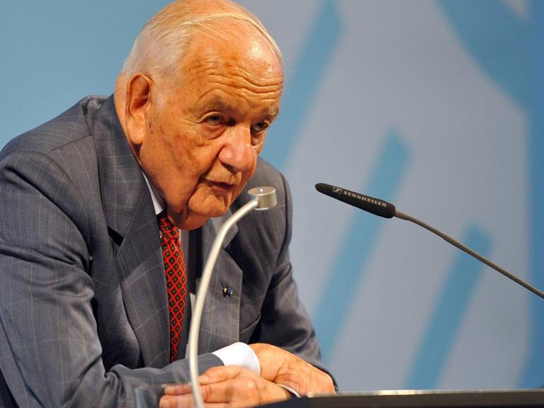 Grosser lehnt an einem Rednerpult und spricht ins Mikrofon