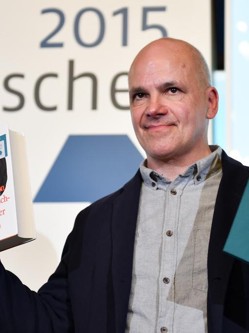 Frank Witzel steht im Römer in Frankfurt am Main mit dem Deutschen Buchpreis 2015 und einem Exemplar seines Buches «Die Erfindung der Roten Armee Fraktion durch einen manisch-depressiven Teenager im Sommer 1969» auf der Bühne.