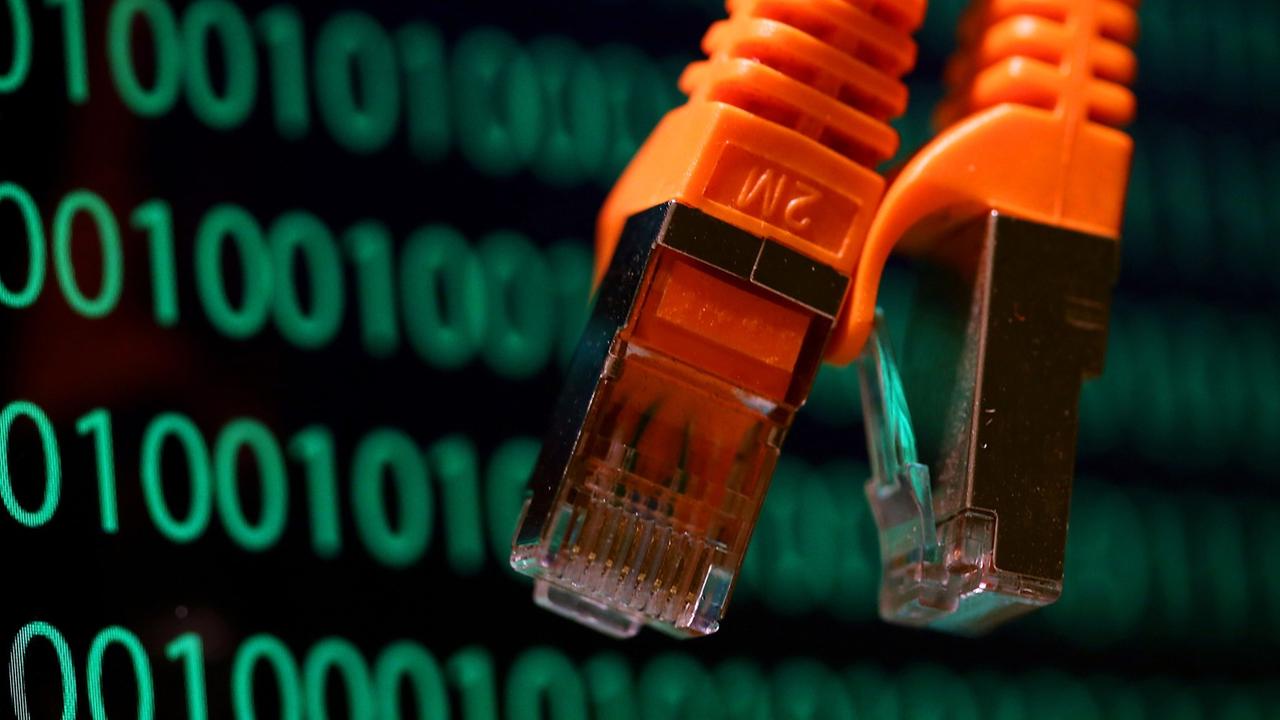 Zwei orangefarbene Netzwerkkabel hängen vor vor einem Computer-Bildschirm, der Zahlenkolonnen mit einem binären Code zeigt. Zwei orangefarbene Netzwerkkabel hängen vor vor einem Computer-Bildschirm, der Zahlenkolonnen mit einem binären Code zeigt.
