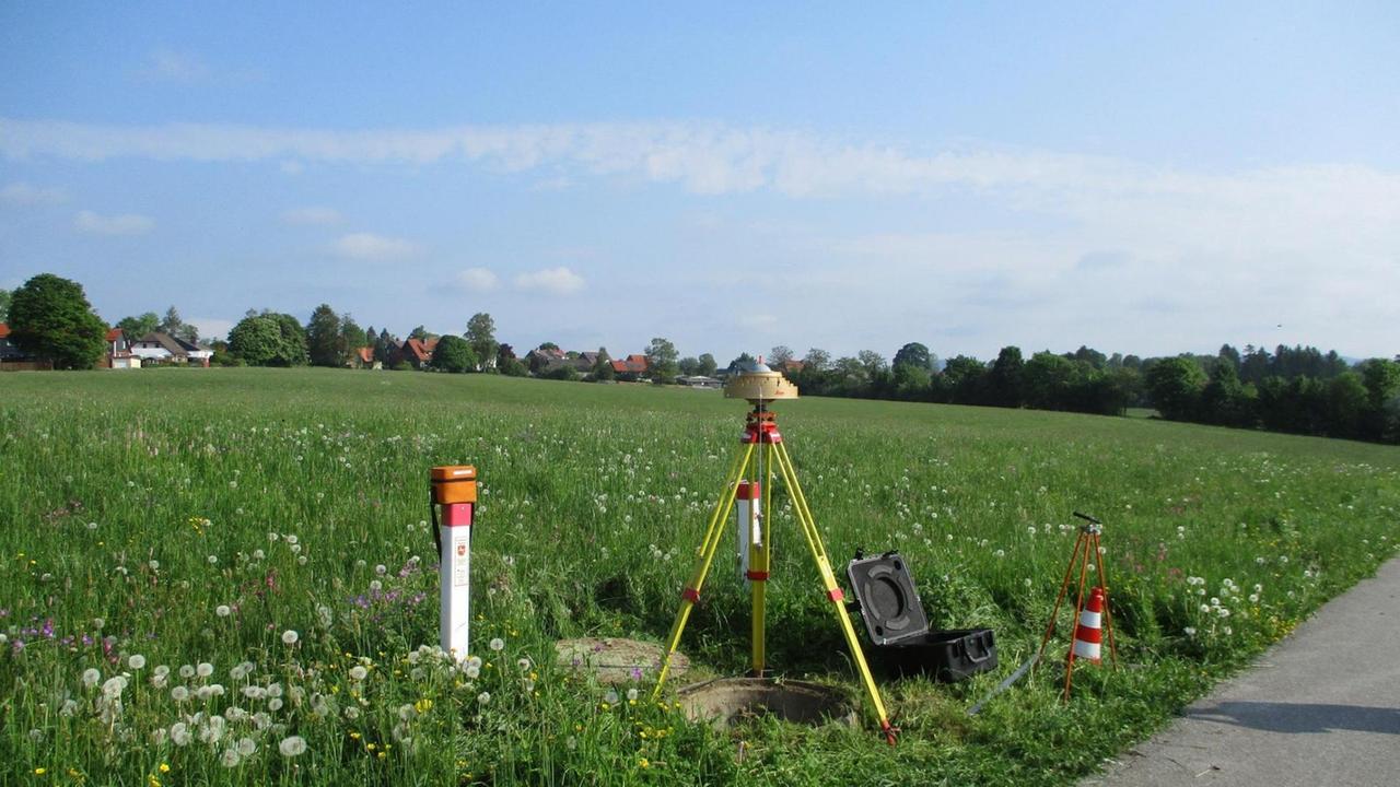 Ein Vermessungsinstrument steht vor einer leicht hügeligen, grünen Landschaft. Ein Vermessungsinstrument steht vor einer leicht hügeligen, grünen Landschaft.