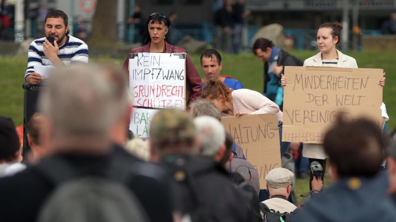 Bei einer Demonstration gegen Corona-Beschränkungen halten Demonstranten Plakate hoch andere schauen dabei zu. Bei einer Demonstration gegen Corona-Beschränkungen halten Demonstranten Plakate hoch andere schauen dabei zu.