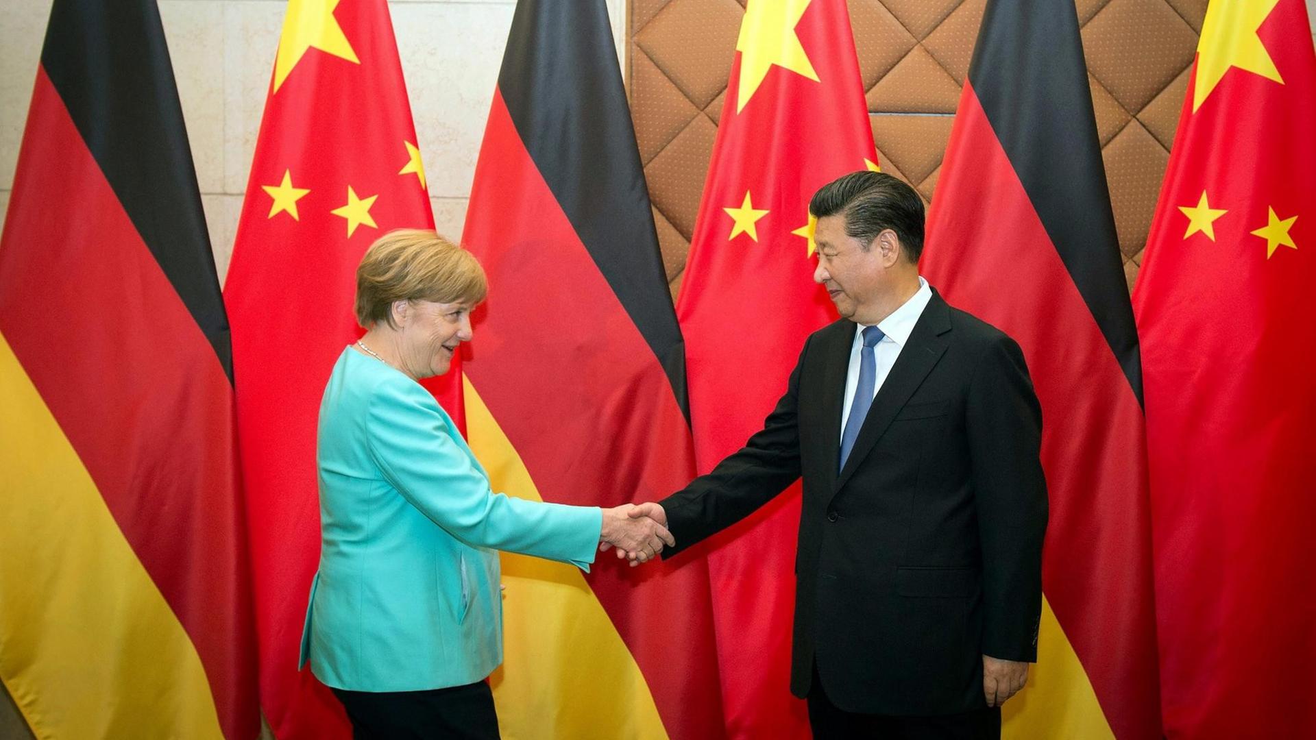 Bundeskanzlerin Angela Merkel und Chinas Präsident Xi Jinping schütteln sich vor den Flaggen ihrer Länder stehend die Hände.