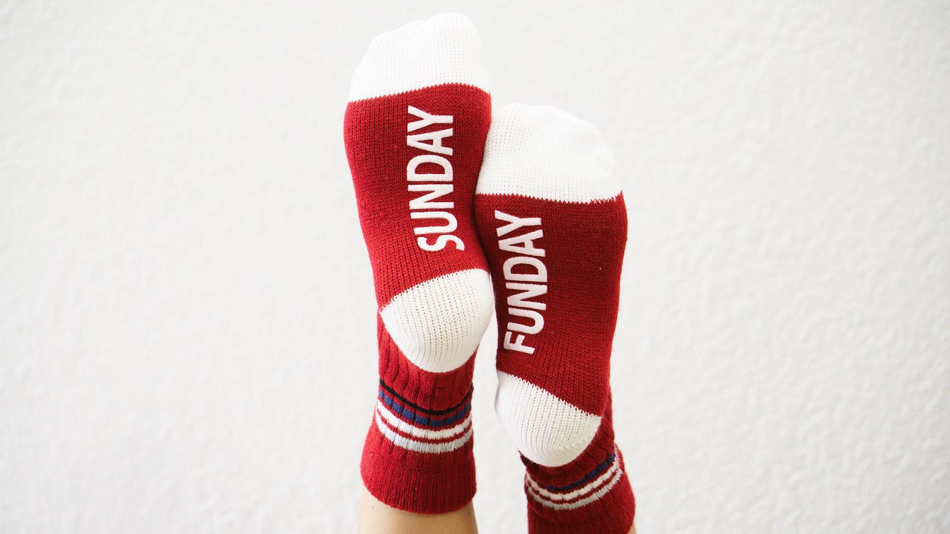 Zwei hochgelegte Füße mit roten Socken und dem Aufdruck "Sonntag" Zwei hochgelegte Füße mit roten Socken und dem Aufdruck "Sonntag"