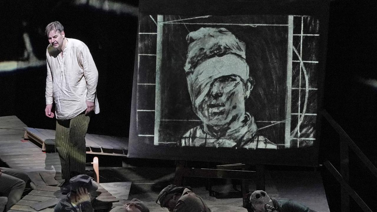 Wozzeck steht auf der Bühne, in seiner Nähe liegen etliche Soldaten auf dem Boden. Wozzeck steht auf der Bühne, in seiner Nähe liegen etliche Soldaten auf dem Boden.