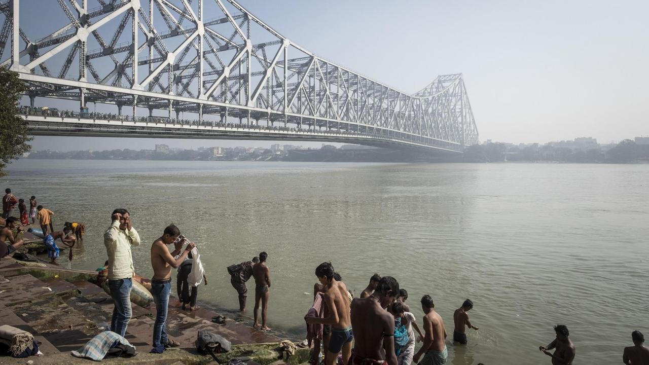 Badende am Ufer des Hugli Flusses, mit dem Blick auf die moderne Stahlkonstruktion der Howrah Brücke. Badende am Ufer des Hugli Flusses, mit dem Blick auf die moderne Stahlkonstruktion der Howrah Brücke.