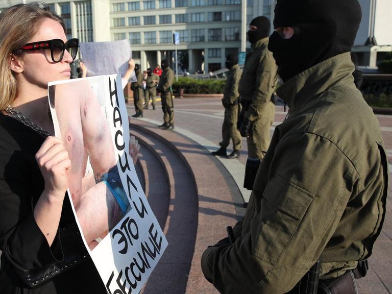 Eine mutige junge Frau steht vor einem Polizisten während der Proteste in Minsk gegen den Präsidenten Lukaschenko. Sie konfrontiert ihn mit einem Plakat, auf dem Wunden eines von der Polizei malträtierten Demonstranten zu sehen sind. Auf dem Plakat steht auf belarussisch: Gewalt ist Schwäche.