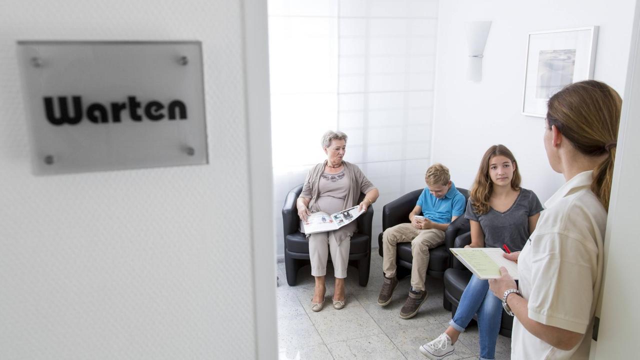 Eine Sprechstundenhilfe ruft einen Patienten aus dem Wartezimmer auf. Eine Sprechstundenhilfe ruft einen Patienten aus dem Wartezimmer auf.