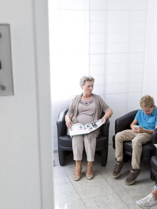 Eine Sprechstundenhilfe ruft einen Patienten aus dem Wartezimmer auf.