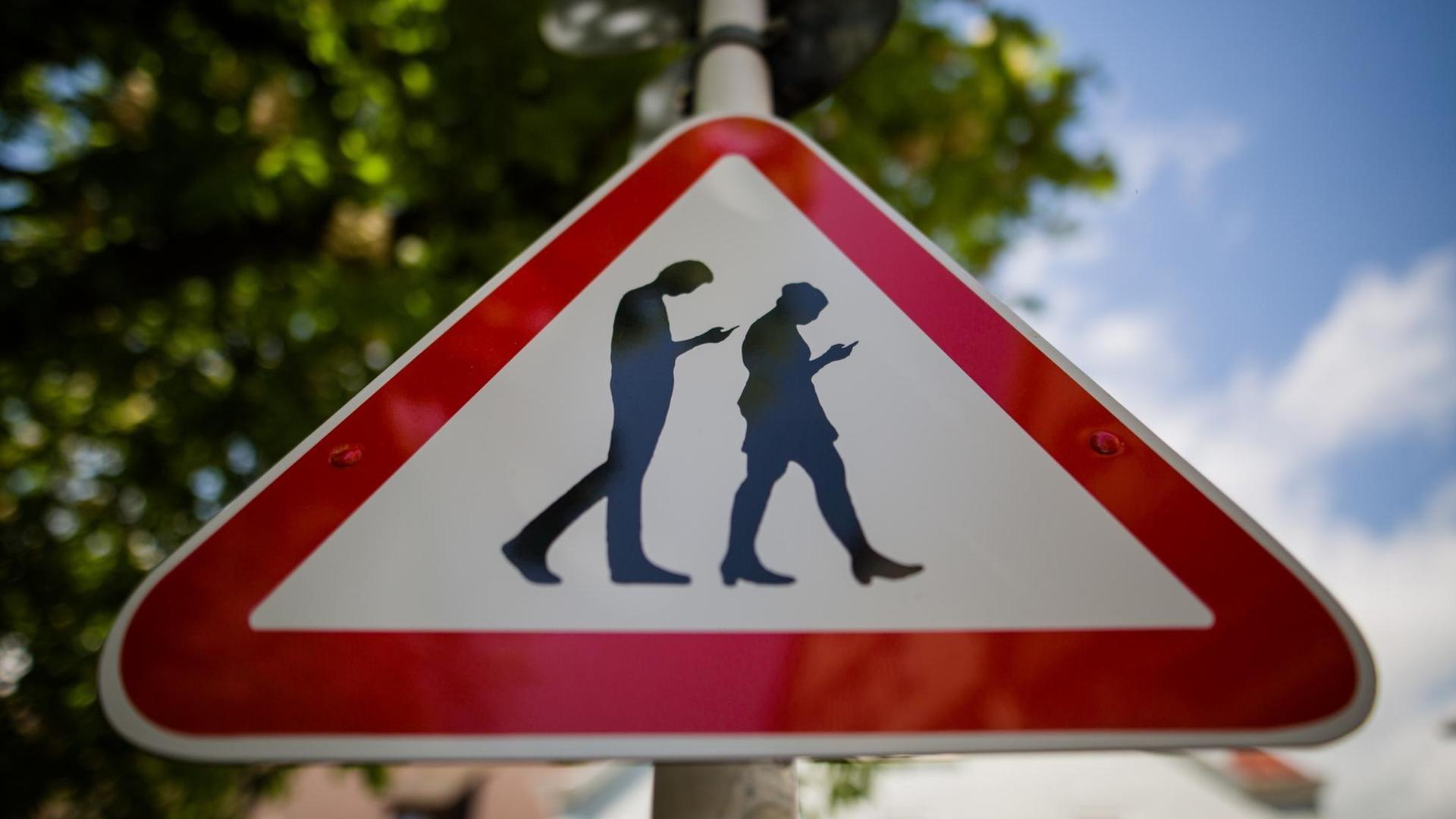 25.04.2018, Baden-Württemberg, Reutlingen: Ein Schild warnt an einer Straße neben einer Schule vor "Smombies". Die Abkürzung ist ein Kunstwort für _Smartphone_ und _Zombie_ und symbolisiert Menschen, die ständig mit dem Blick auf das Smartphone über die Straßen laufen. Foto: Christoph Schmidt/dpa | Verwendung weltweit 25.04.2018, Baden-Württemberg, Reutlingen: Ein Schild warnt an einer Straße neben einer Schule vor "Smombies". Die Abkürzung ist ein Kunstwort für _Smartphone_ und _Zombie_ und symbolisiert Menschen, die ständig mit dem Blick auf das Smartphone über die Straßen laufen. Foto: Christoph Schmidt/dpa | Verwendung weltweit