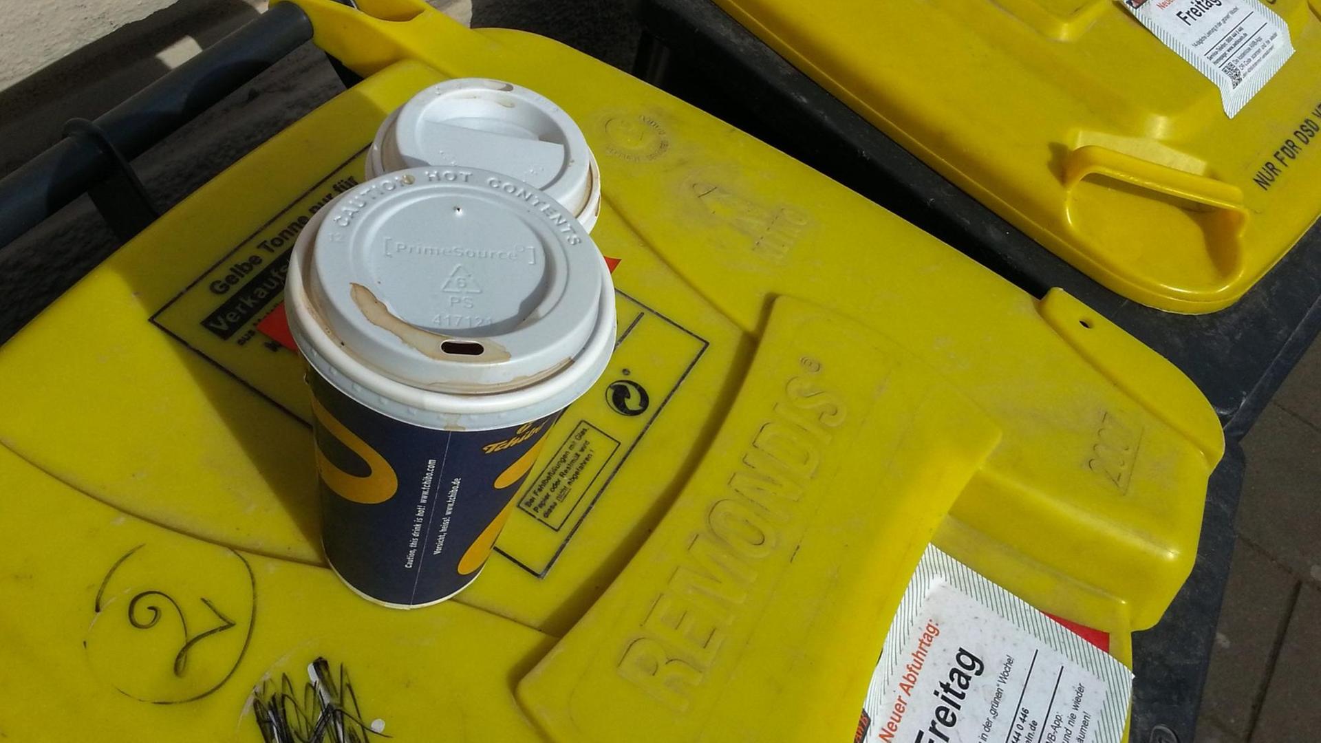 Auf der gelben Tonne für Plastikmüll hat jemand zwei leere Kaffeebecher aus Pappe deponiert. Aufgenommen in Köln. Auf der gelben Tonne für Plastikmüll hat jemand zwei leere Kaffeebecher aus Pappe deponiert. Aufgenommen in Köln.