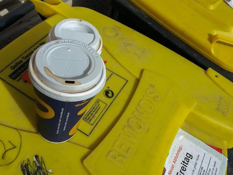 Auf der gelben Tonne für Plastikmüll hat jemand zwei leere Kaffeebecher aus Pappe deponiert. Aufgenommen in Köln.