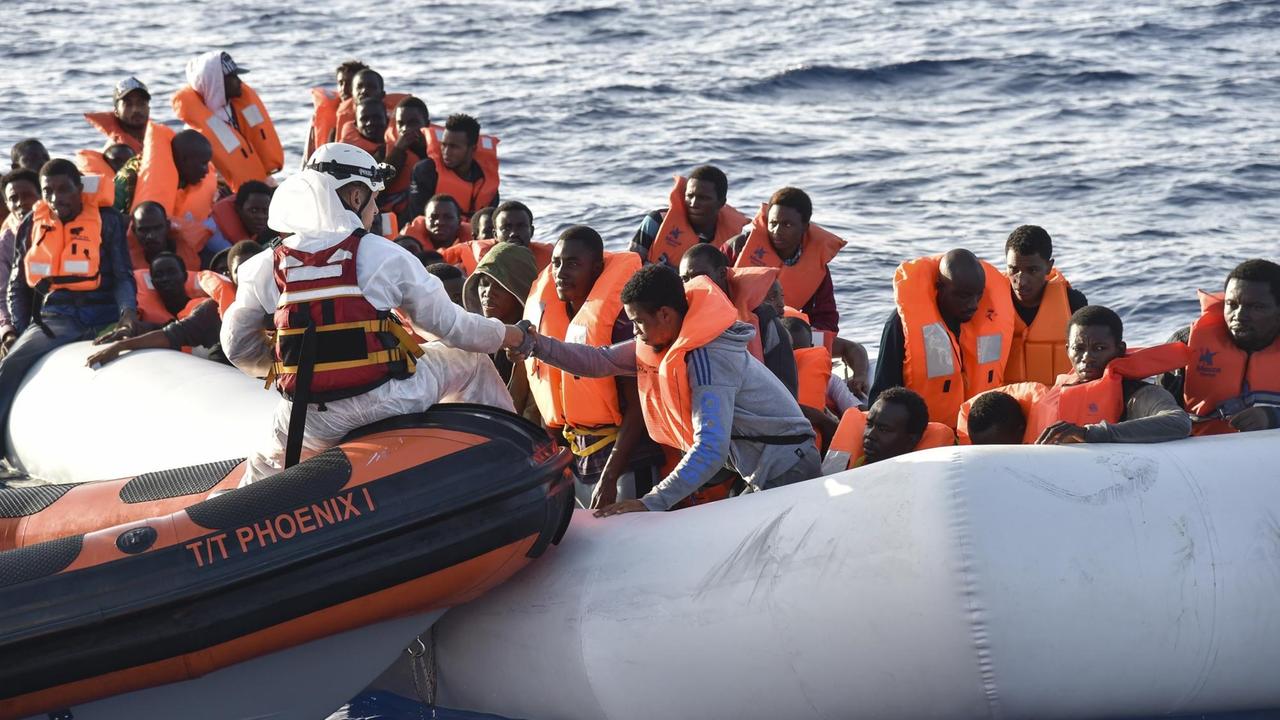 Mitglieder der Maltesischen NGO-Organisation MOAS helfen am 3.11.2016 Flüchtlingen an Bord eines kleinen Rettungsbootes während einer gemeinsamen Rettungsaktion mit dem Italienischen Roten Kreuz vor der Küste Libyens. Mitglieder der Maltesischen NGO-Organisation MOAS helfen am 3.11.2016 Flüchtlingen an Bord eines kleinen Rettungsbootes während einer gemeinsamen Rettungsaktion mit dem Italienischen Roten Kreuz vor der Küste Libyens.