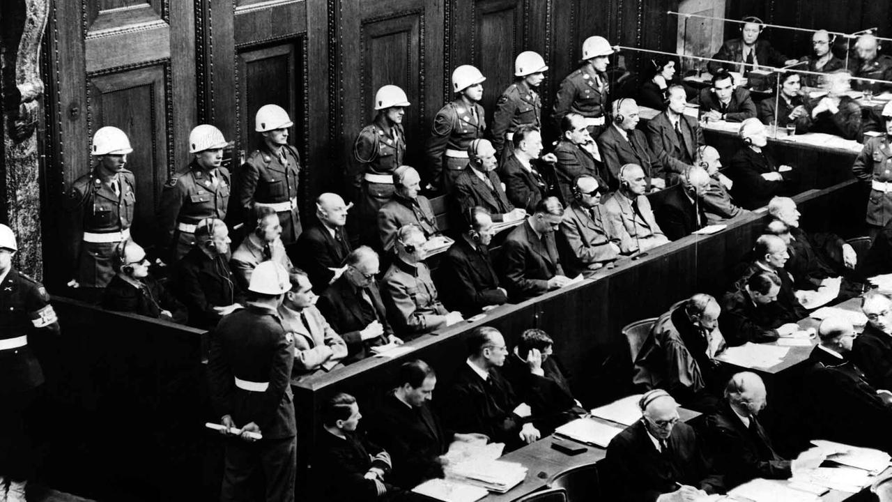 Blick auf die Anklagebank beim Kriegsverbrecherprozess in Nürnberg, 18.03.1946. Die Angeklagten schauen interessiert zum Zeugenstand (nicht im Bild) in dem im Moment dieser Aufnahme gerade Hermann Göring saß und seine Aussage machte. 