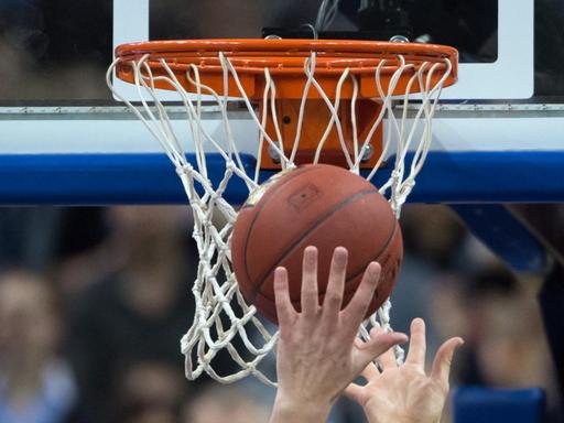 Hände recken sich unter einem Basketballkorb nach dem Ball.