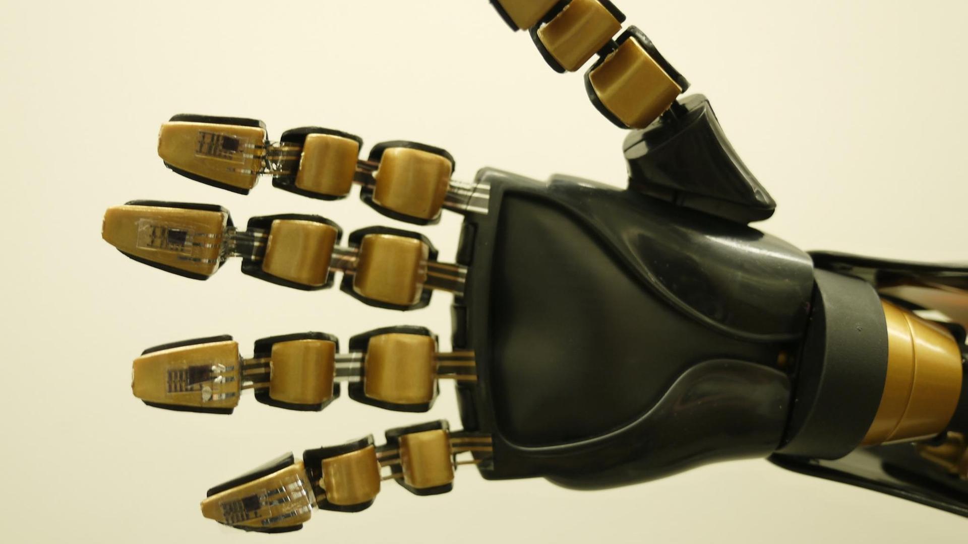 Eine künstliche Hand, bestehend aus mehreren goldfarbenen Elementen und schwarzem Plastik Eine künstliche Hand, bestehend aus mehreren goldfarbenen Elementen und schwarzem Plastik
