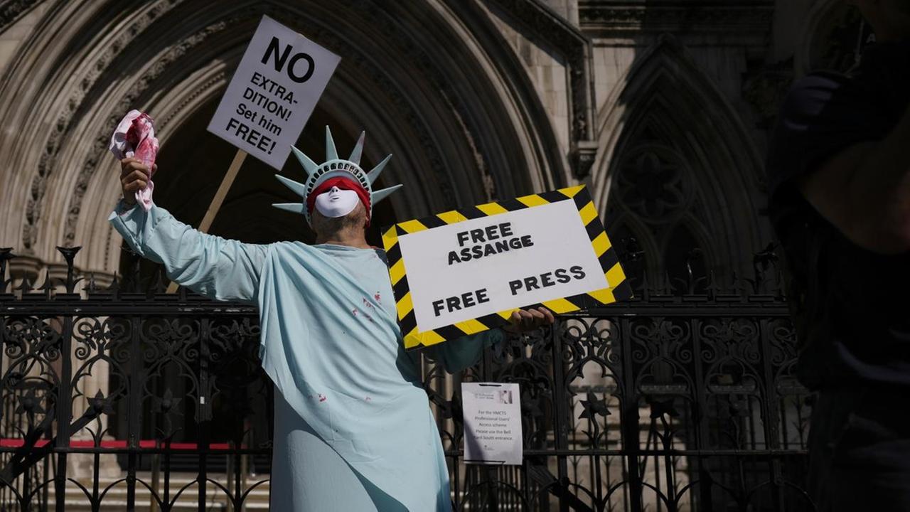 Ein als Freiheitsstatue verkleideter Mann hält ein Schild hoch, auf dem "Free Assange. Free Press" steht Ein als Freiheitsstatue verkleideter Mann hält ein Schild hoch, auf dem "Free Assange. Free Press" steht