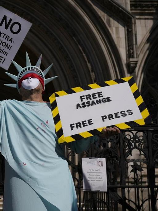 Ein als Freiheitsstatue verkleideter Mann hält ein Schild hoch, auf dem "Free Assange. Free Press" steht