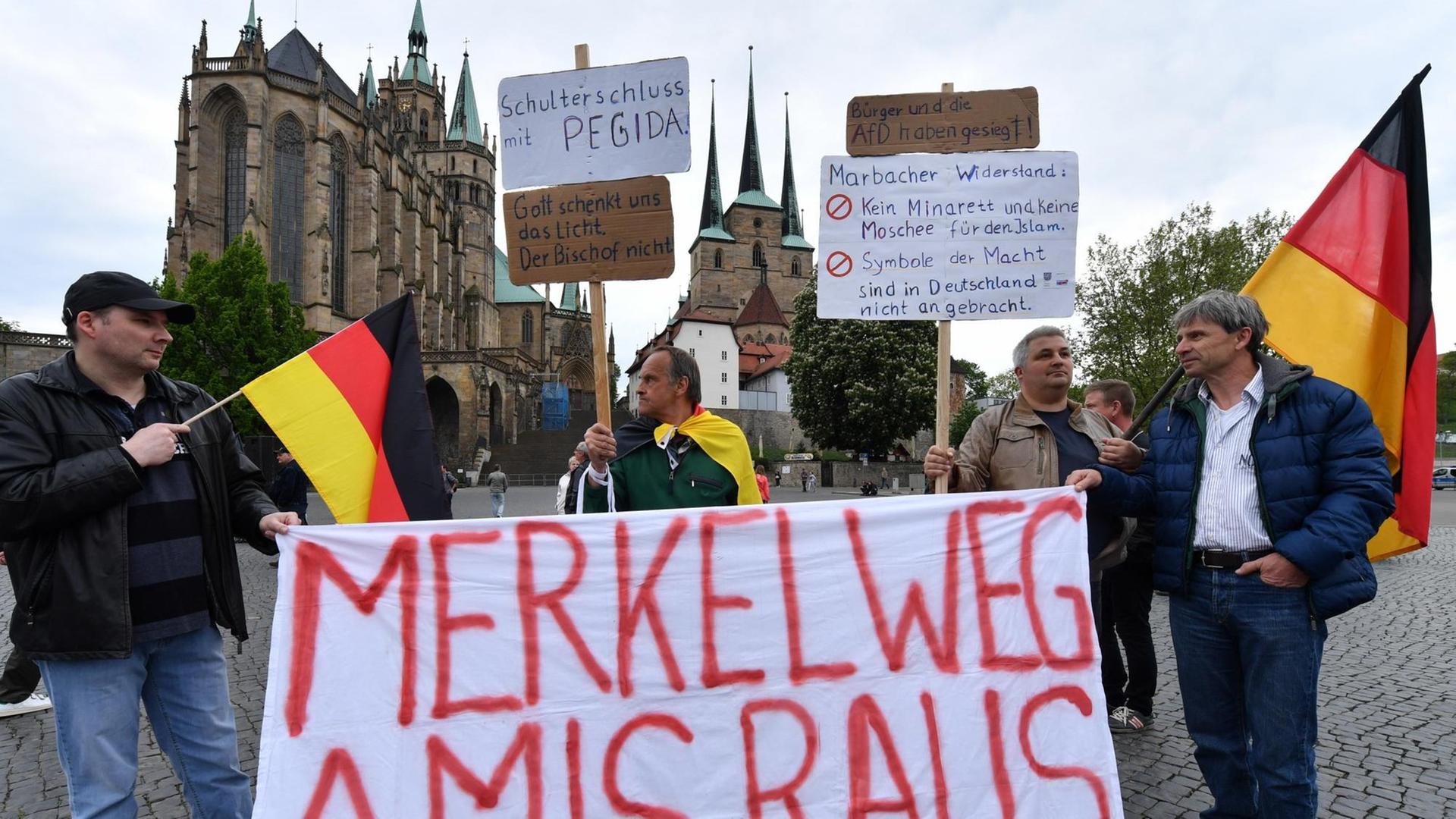 Demonstranten stehen auf dem Domplatz in Erfurt (Thüringen) bei einer Kundgebung der Alternative für Deutschland (AfD) gegen die Asyl- und Integrationspolitik von Bundes- und Landesregierung mit einem Banner mit der Aufschrift: "Merkel weg Amis raus". Demonstranten stehen auf dem Domplatz in Erfurt (Thüringen) bei einer Kundgebung der Alternative für Deutschland (AfD) gegen die Asyl- und Integrationspolitik von Bundes- und Landesregierung mit einem Banner mit der Aufschrift: "Merkel weg Amis raus".