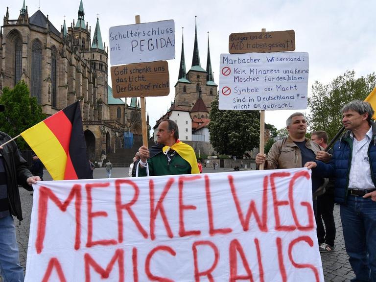 Demonstranten stehen auf dem Domplatz in Erfurt (Thüringen) bei einer Kundgebung der Alternative für Deutschland (AfD) gegen die Asyl- und Integrationspolitik von Bundes- und Landesregierung mit einem Banner mit der Aufschrift: "Merkel weg Amis raus".