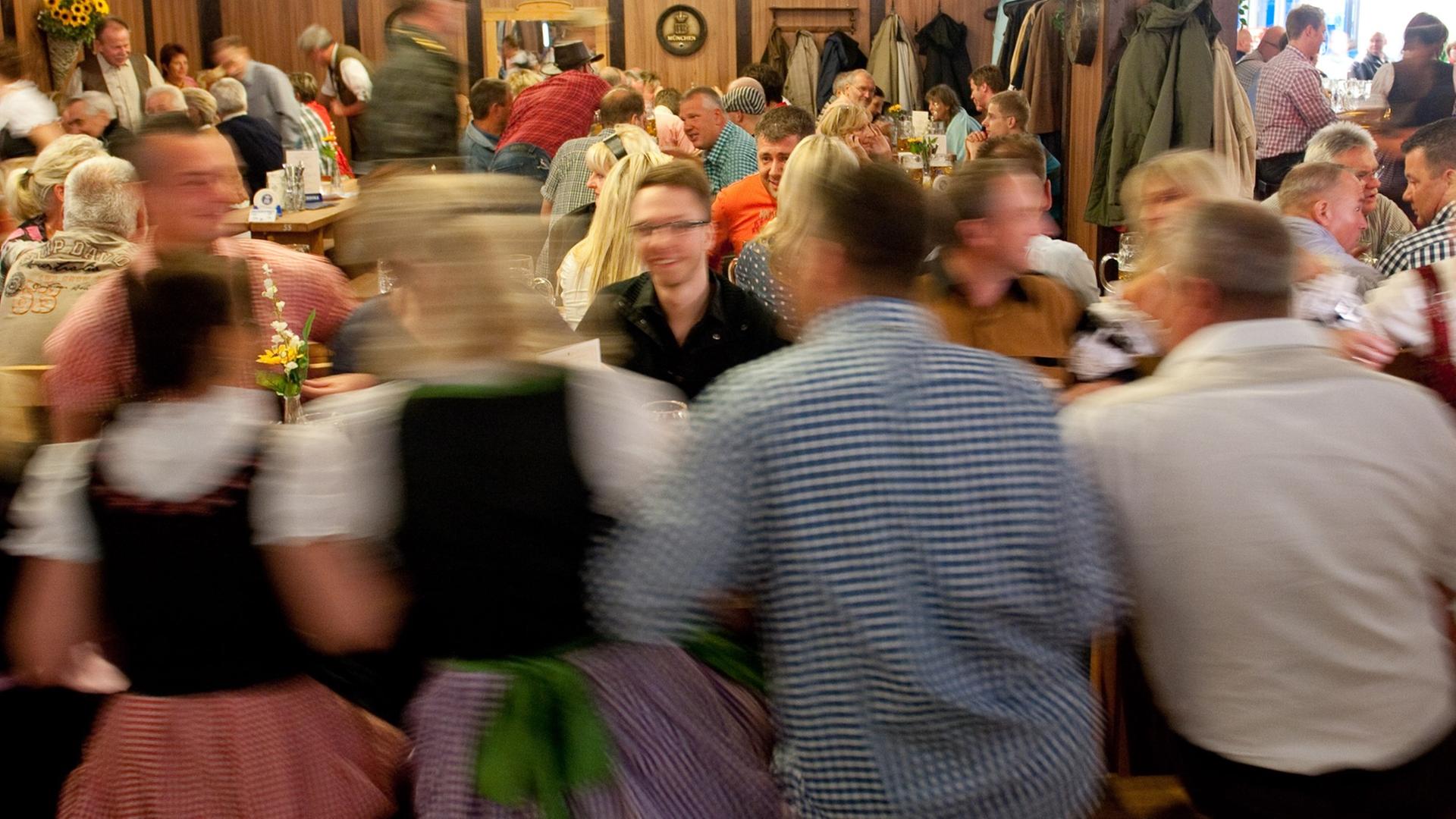 Menschen sitzen um Tische auf Bänken und Schunkeln, Frauen tragen Dirndl Menschen sitzen um Tische auf Bänken und Schunkeln, Frauen tragen Dirndl