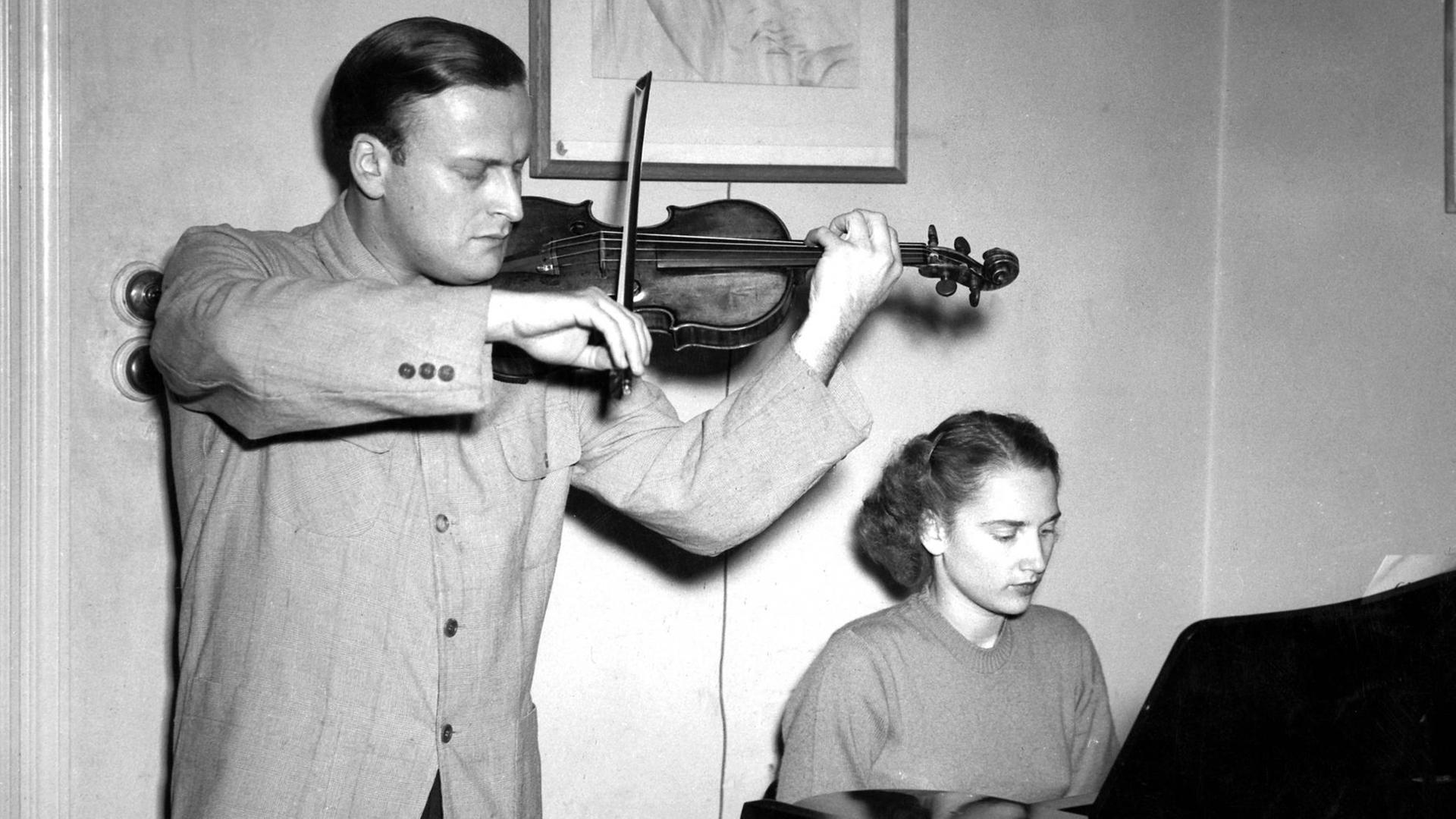 Eine Frau sitzt an einem Klavier. Neben ihr steht ein Mann und spielt Geige. Eine Frau sitzt an einem Klavier. Neben ihr steht ein Mann und spielt Geige.