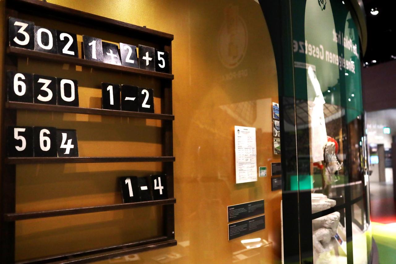 Hinter einer Glaswand im Fußballmuseum in Dortmund ist die Liedtafel aus Bad Nauheim mit schwarzen Nummerplättchen in einem Holzrahmen.