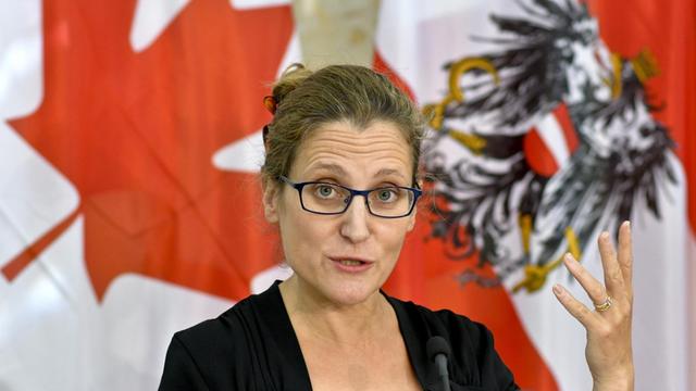 Eine junge Frau mit Brille vor einer kanadischen Flagge.