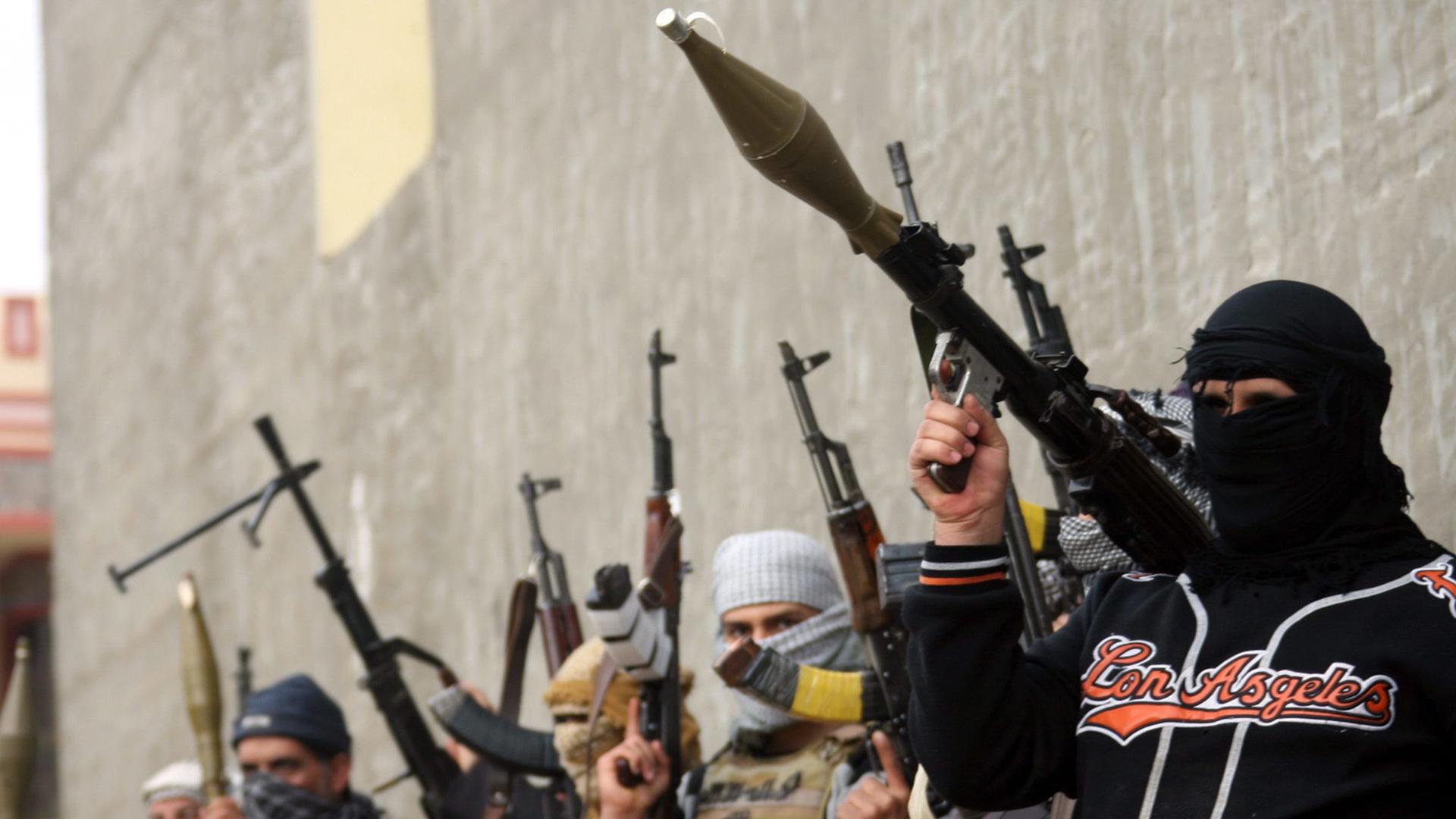 Vermummte, mit Raketenwerfern und Maschinengewehren bewaffnete Männer stehen vor einer Mauer. Vermummte, mit Raketenwerfern und Maschinengewehren bewaffnete Männer stehen vor einer Mauer.