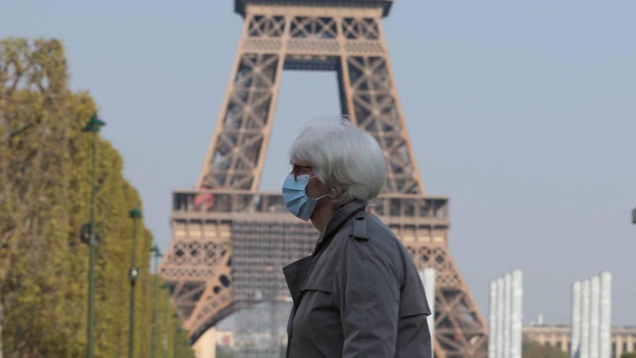 Eine Frau mit Mund-Nase-Schutz vor dem Pariser Eiffelturm