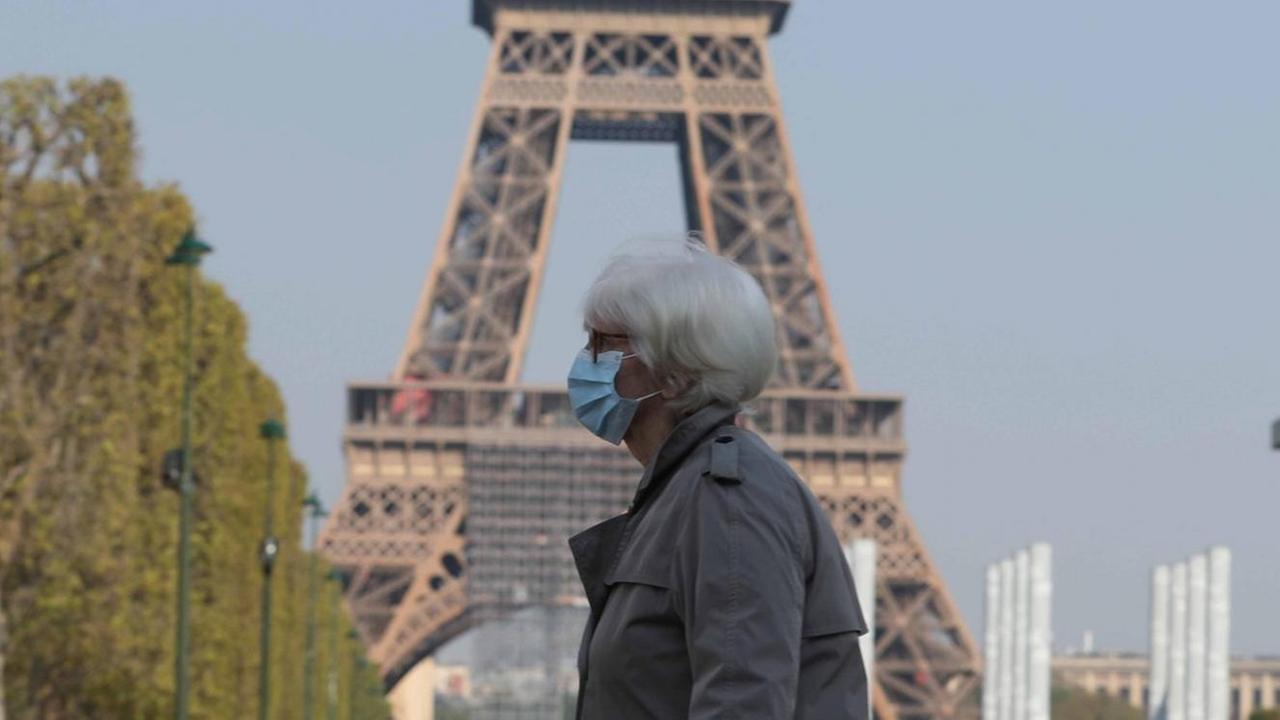 Eine Frau mit Mund-Nase-Schutz vor dem Pariser Eiffelturm Eine Frau mit Mund-Nase-Schutz vor dem Pariser Eiffelturm