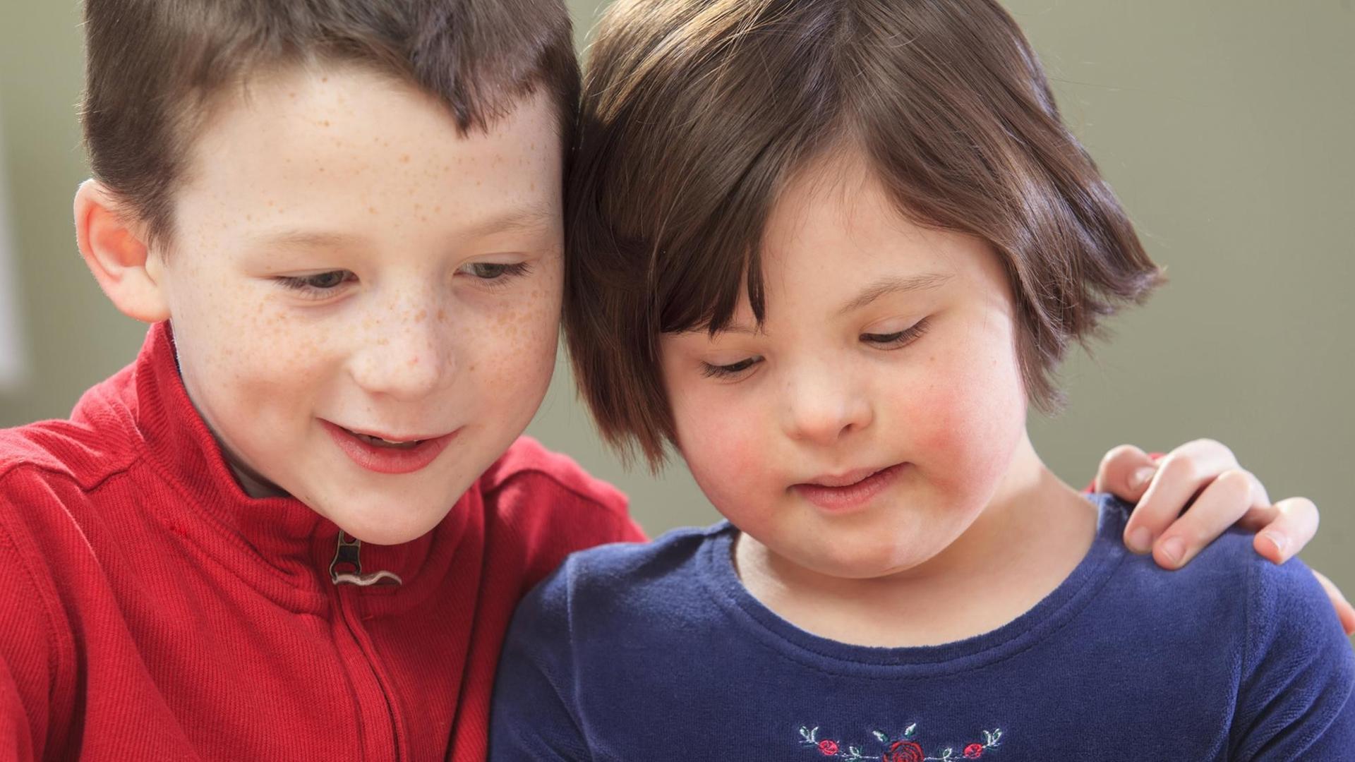 Eine Junge sitzt neben seiner jungen Schwester, die das Downsyndrom hat. Eine Junge sitzt neben seiner jungen Schwester, die das Downsyndrom hat.