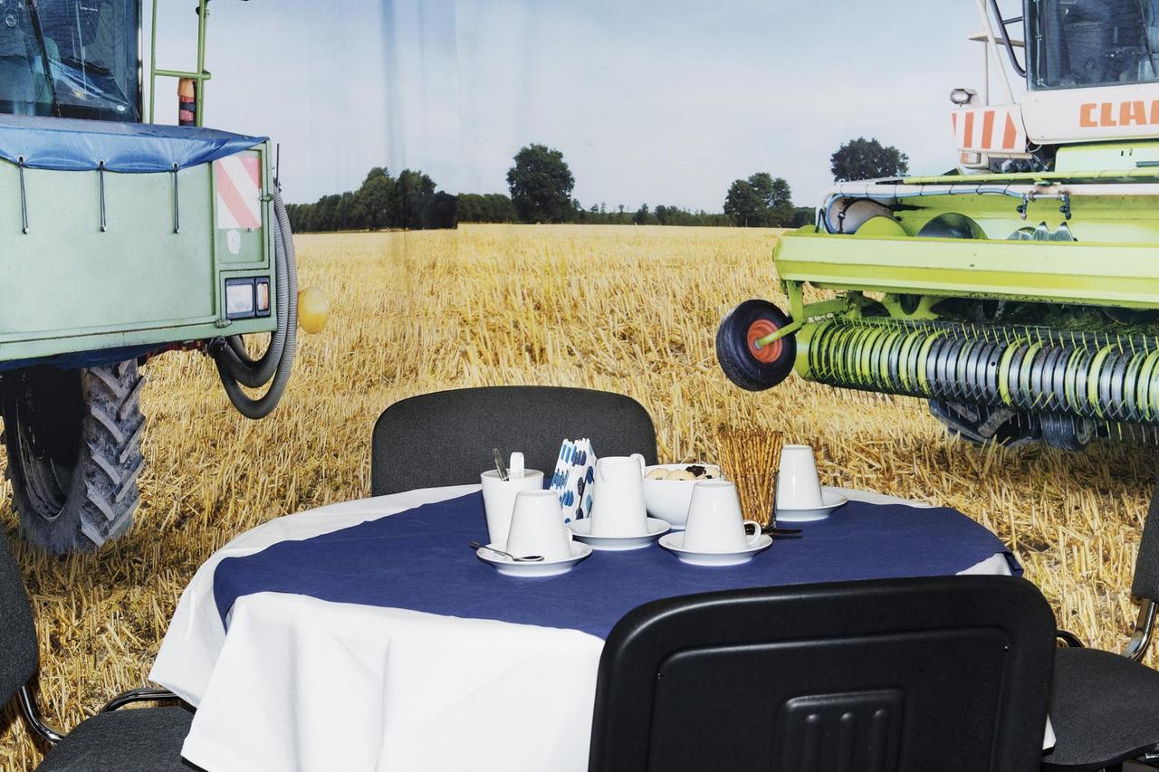Vor einer Fotwand von einem Feld mit Mähdreschern steht ein Messetisch mit Kaffee.